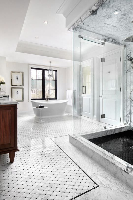 حمام بزرگ و لوکسی که وان سفید زیبا، پارتیشن شیشه ای دوش گرفتن و کفپوش سنگی مربع شکل دارد
